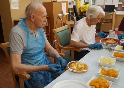 Two residents seated at a table making fruit kebabs