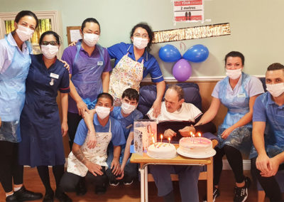 Resident surrounded by staff with to birthday cakes at Princess Christian